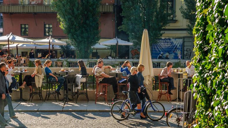 ljudje sedijo v lokalih ob Ljubljanici